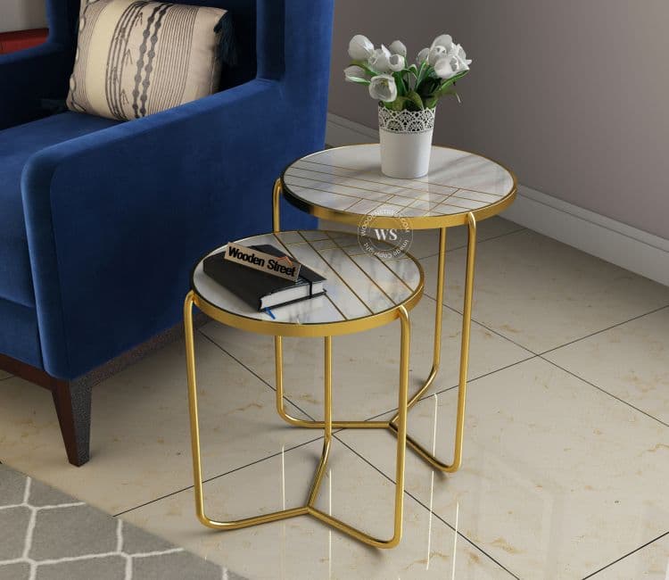 Set of two round marble-top nesting tables with golden frames beside a blue armchair.
