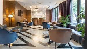 Modern hotel lounge with round tables, blue and beige chairs, and large windows.