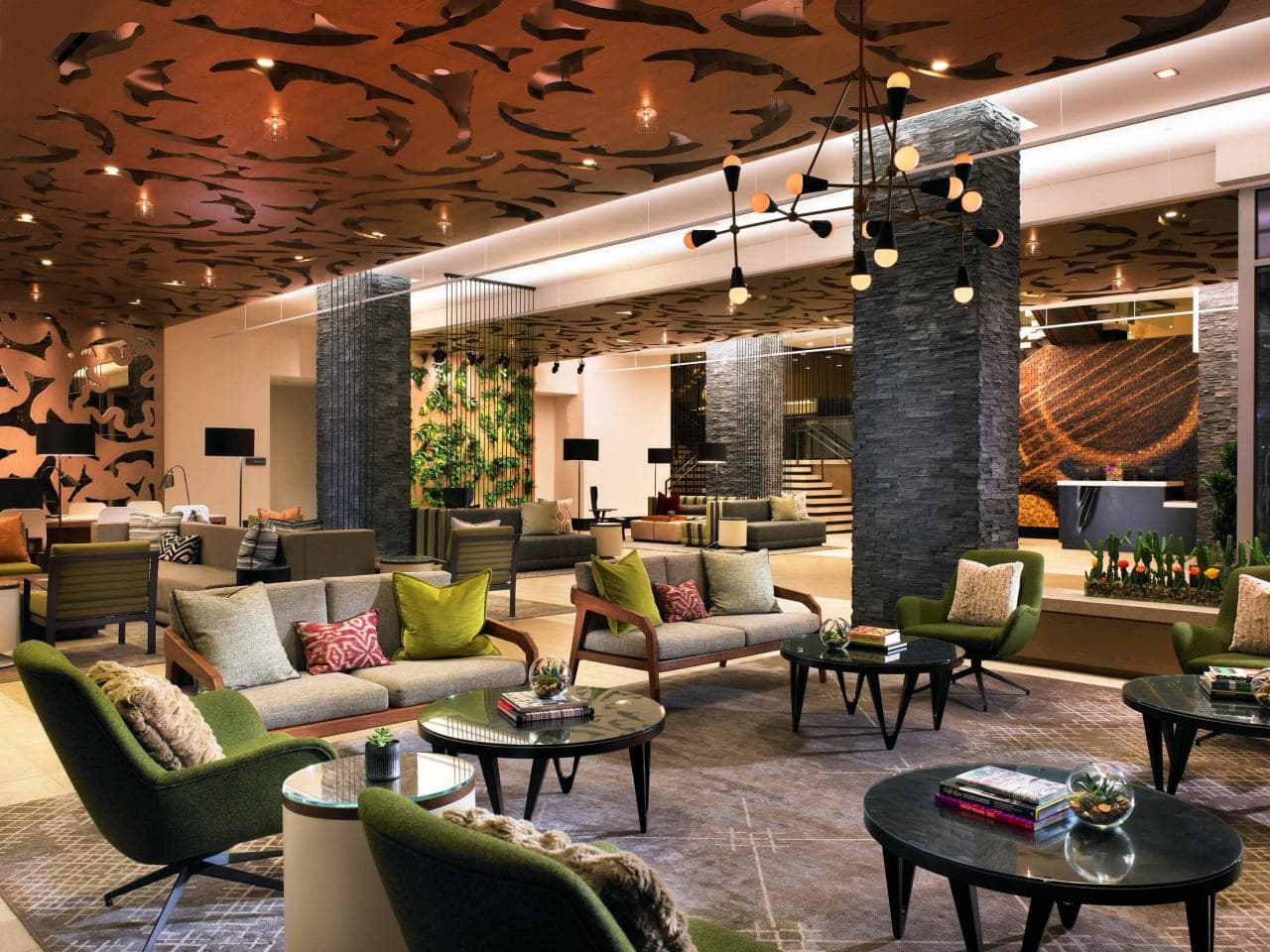Chic hotel lounge with green chairs, modern sofas, round tables, and artistic ceiling design.