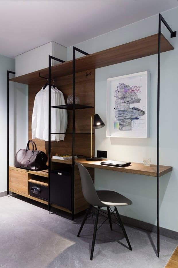 Open wardrobe with hanging shirt, bag, safe, mini fridge, and compact desk setup with chair and lamp.