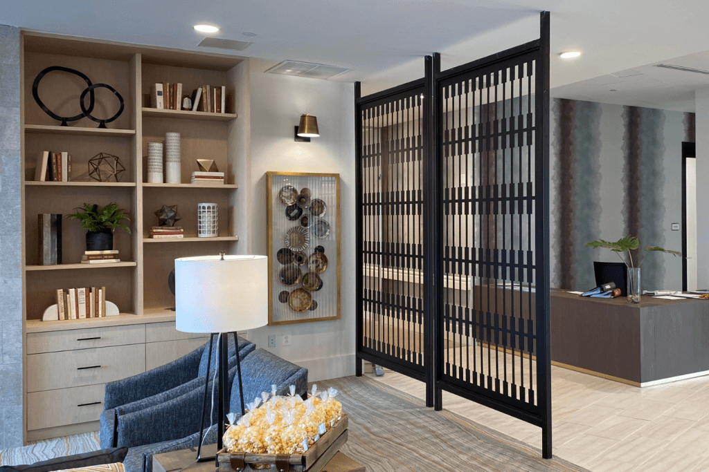 Modern black metal partition with vertical slats separates a cozy lounge area from a reception desk in a stylish office interior.