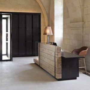 Minimalist stone-clad reception desk with dark wood accents in a modern lobby with arched architecture.