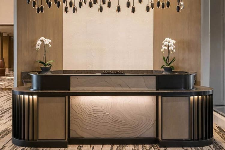 Elegant concierge desk with curved edges, layered wood textures, and orchid decor in a contemporary hotel lobby.