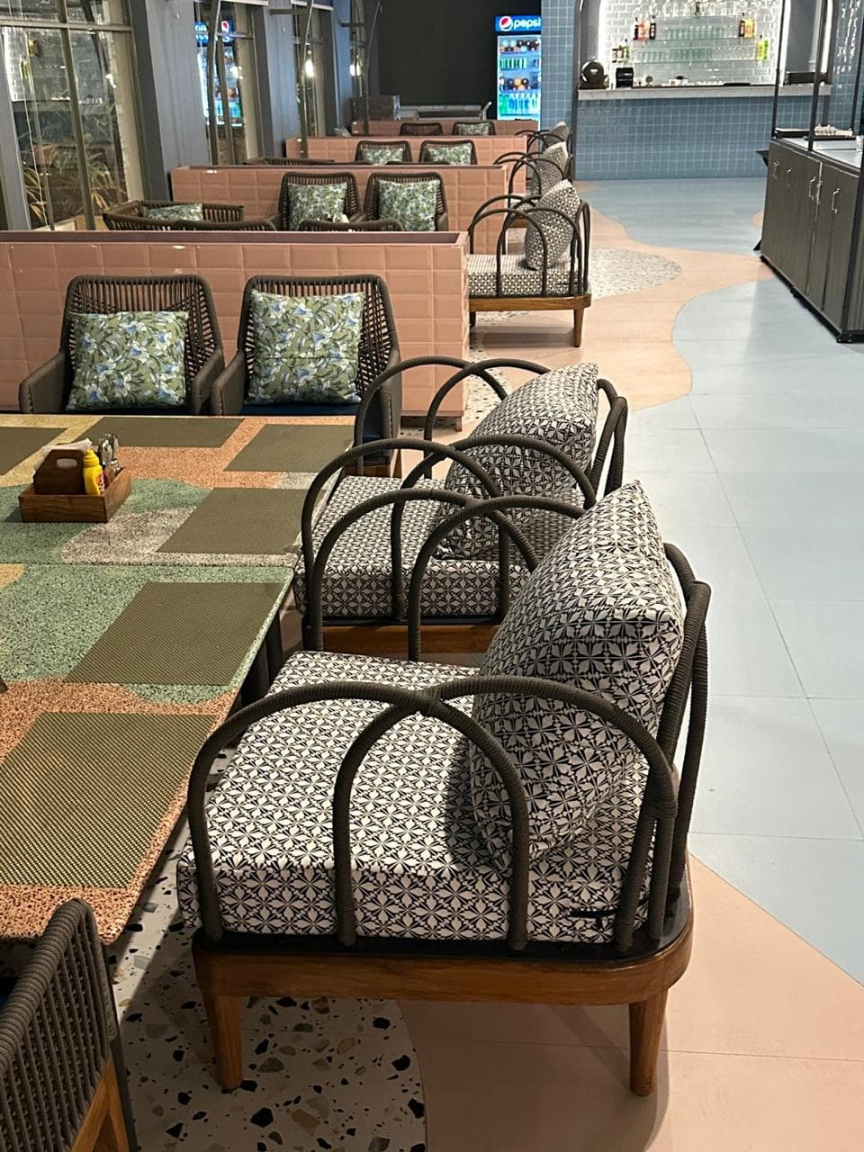 Stylish restaurant seating with patterned cushioned armchairs, terrazzo flooring, and booth-style rope chairs in the background.