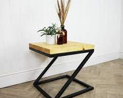 A Z-shaped side table with a natural wood top and black metal frame, adorned with a small plant and dried floral arrangement.