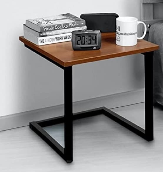 Minimalist bedside table with a wooden top and black metal frame, featuring books, a clock, a mug, and a tablet.