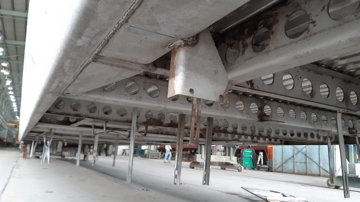 Sturdy Close-up view of a metal underframe structure with perforated beams and welded brackets in an industrial workshop setting.