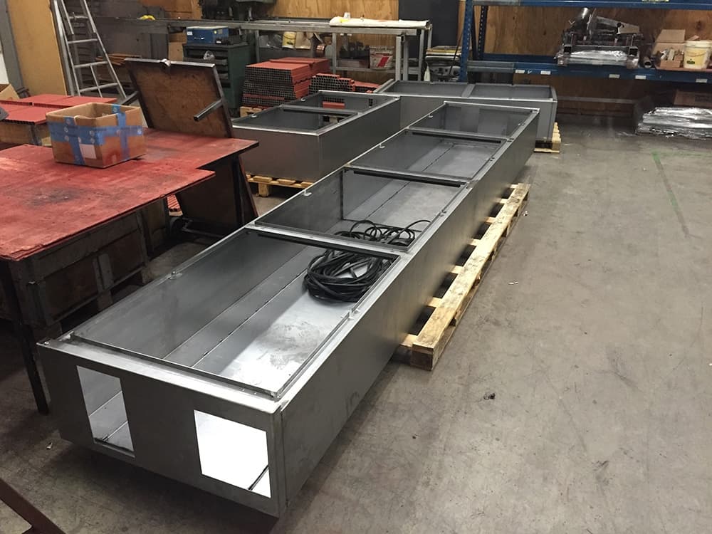 A large, rectangular, sheet metal-based machine frame with cutouts, placed on wooden pallets in an industrial workshop. .