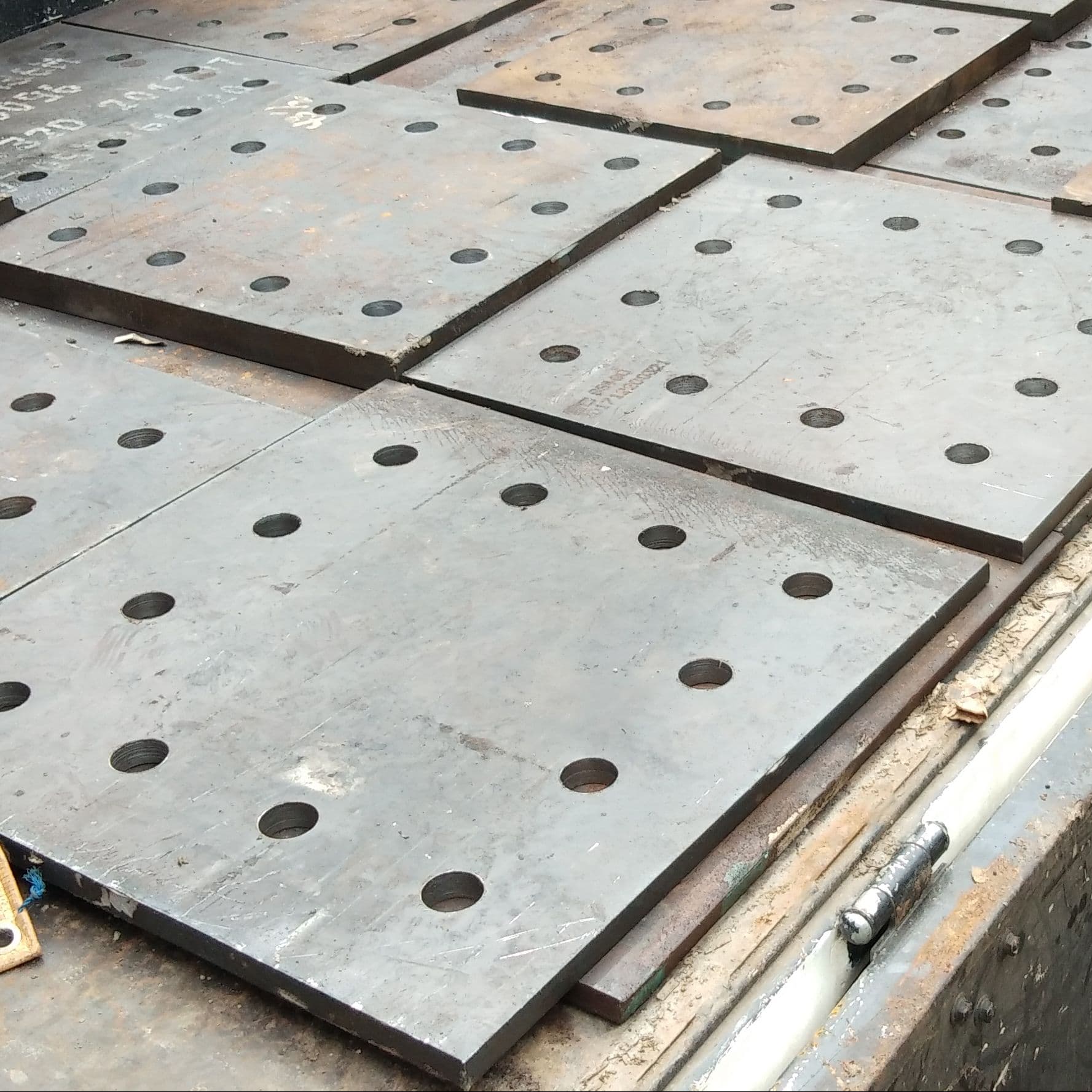 Steel support plates with evenly spaced holes stacked on a metal surface.