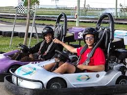 Two young riders in go-karts ready to race on a track, wearing helmets and safety gear.