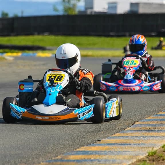 Two racers in colorful go-karts speeding on a track during a competitive race.