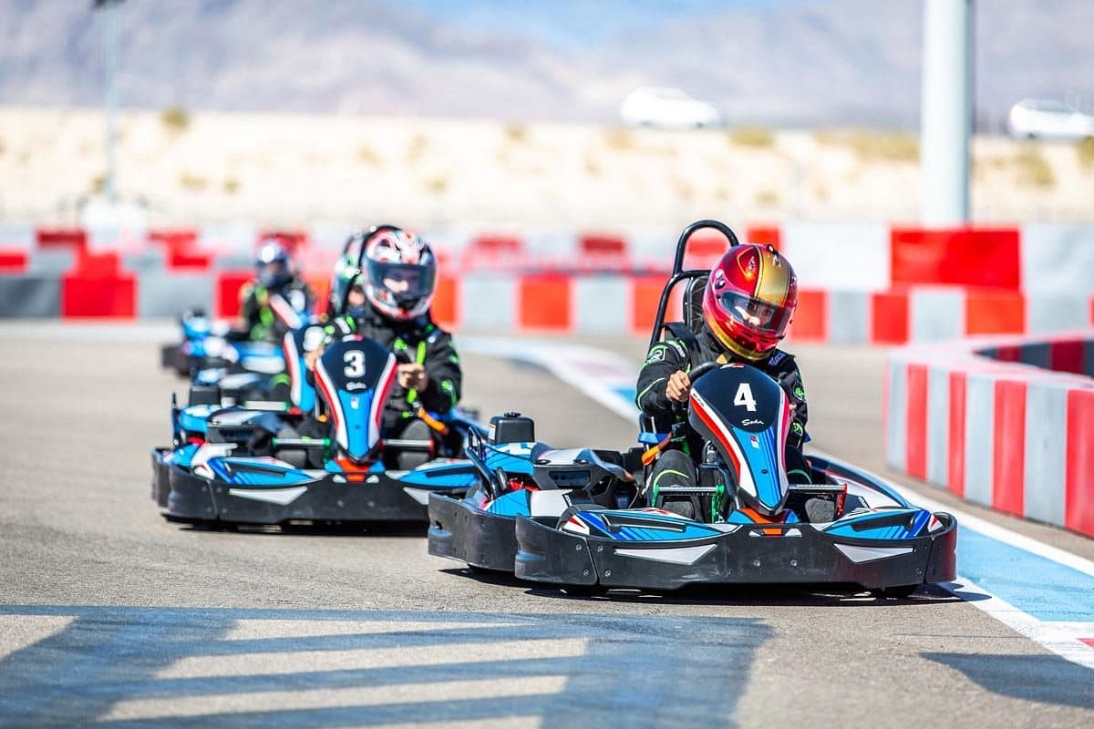 Go-kart racers driving on an outdoor track lined with red and white barriers.
