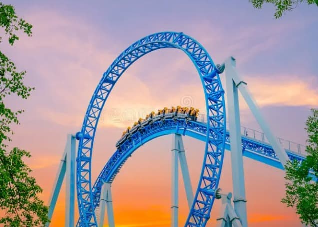 Blue steel roller coaster track with riders looping against a vibrant sunset sky.
