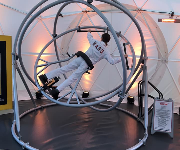 Person in astronaut suit using an indoor human gyroscope trainer ride.