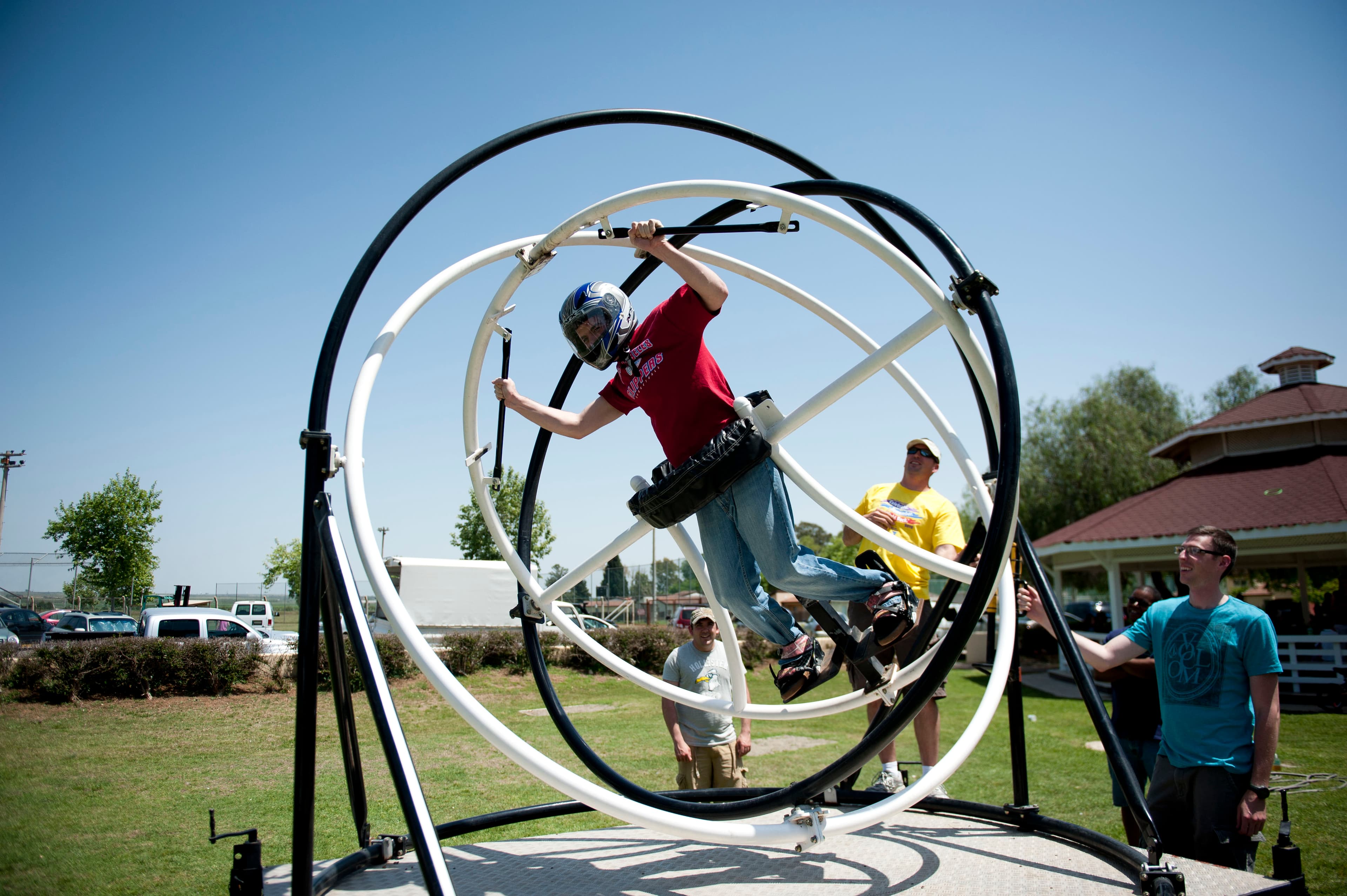 Person strapped into a human gyroscope ride spinning in multiple directions outdoors.