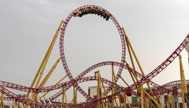 Roller coaster with a red track and yellow supports, carrying riders upside down through a vertical loop.