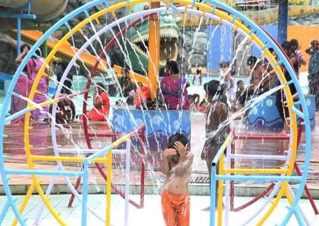 Child enjoying a colorful circular water sprinkler structure at a water park, with streams of water spraying from all directions.