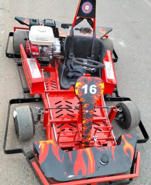 Close-up of a red go-cart featuring bold flame graphics, a padded black seat, and the number 16 prominently displayed on the front panel.