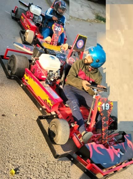 Two red go-carts with flame graphics, numbered 19 and 20, driven by helmeted riders on a sunny road, ready for an exciting race.