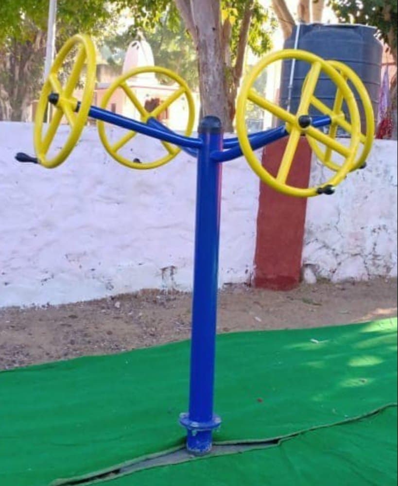 Outdoor hand rotator fitness equipment with a blue frame and yellow rotating wheels, installed on a green mat in an open area.
