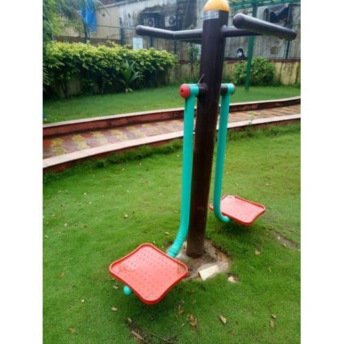 Outdoor fitness equipment with a pendulum swing design, featuring two footrests and handles, installed in a park setting.