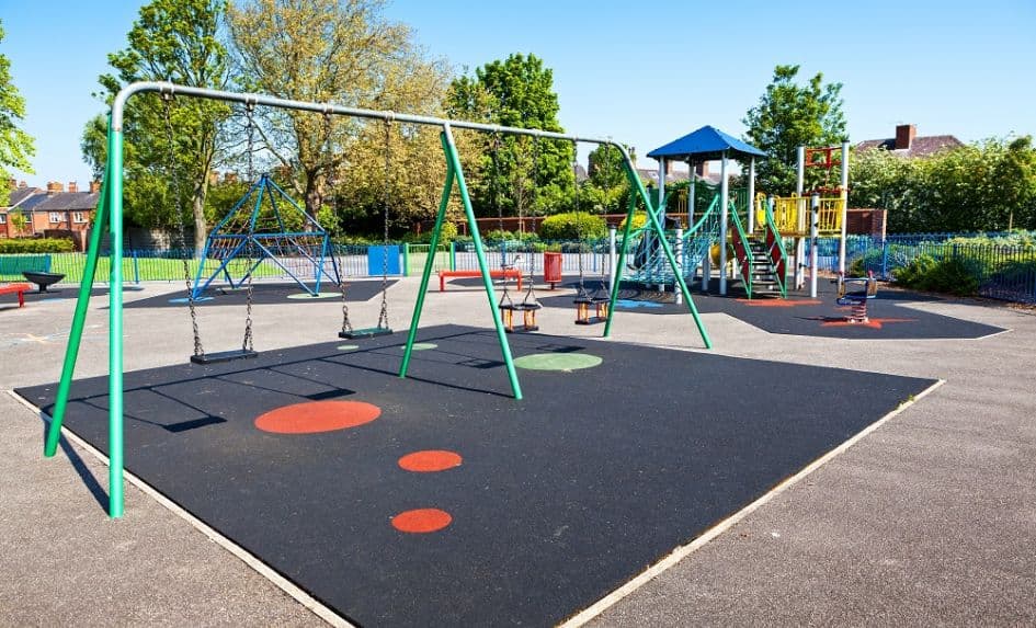 Empty playground with swings, climbing frames, and slides on a sunny day.