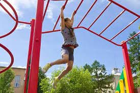 Child playing on red monkey bars in a sunny outdoor playground.