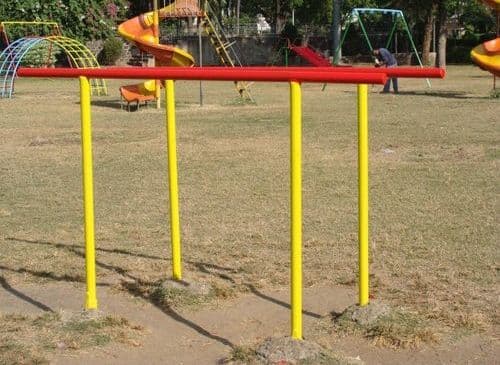 Outdoor parallel bars with red beams and yellow poles in a playground surrounded by grass and other play structures.